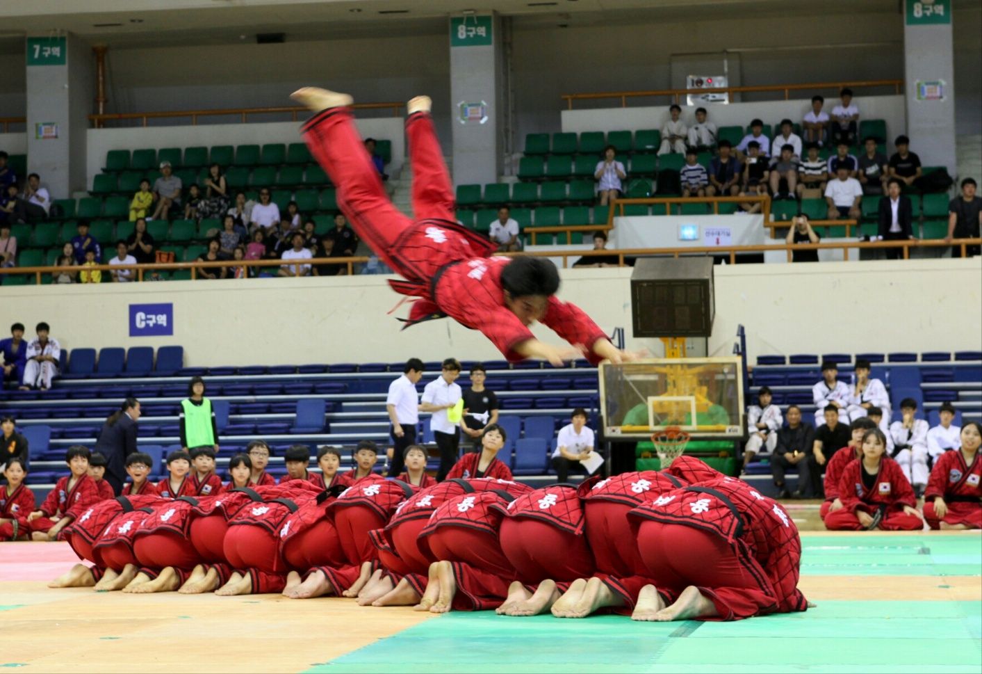 身着红色道服的武者在跪伏学员上方表演空中倒地技